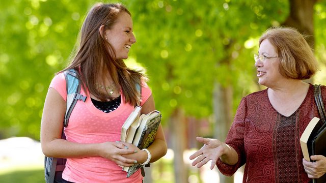 Female student talking to a female professor on the campus mall
