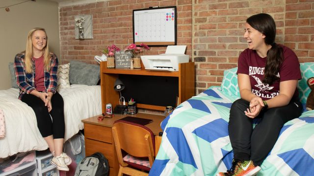 Two female students sitting on beds in a dorm room