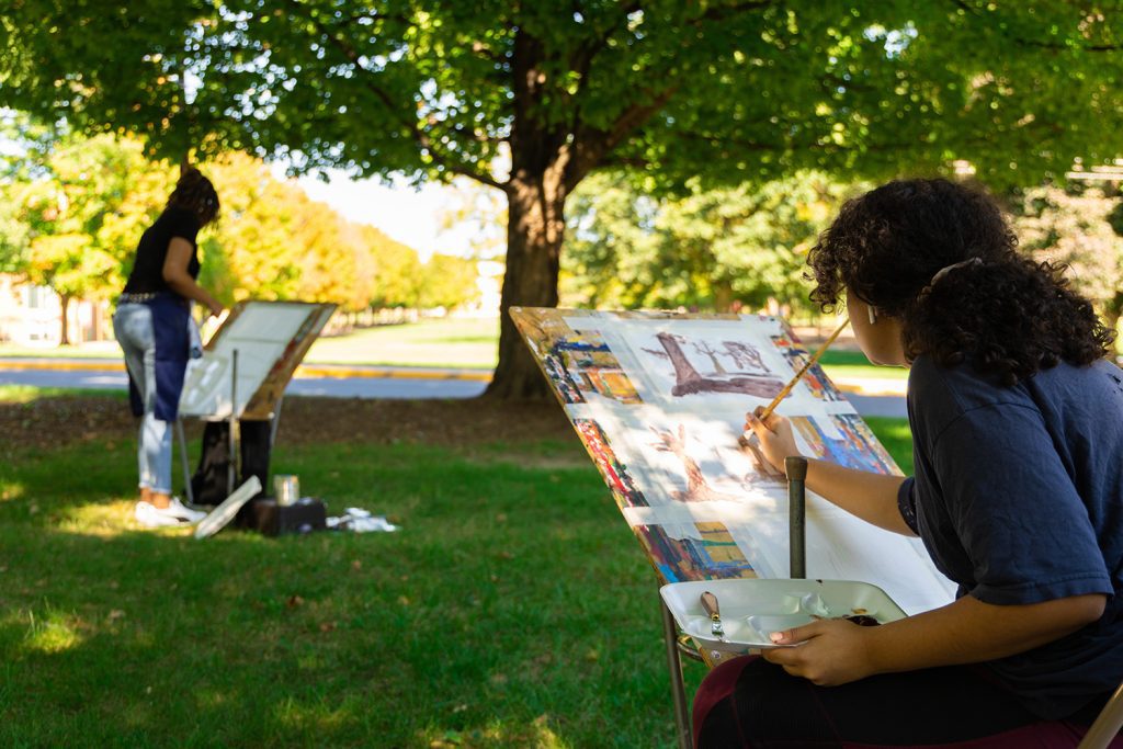 Two students painting artwork outside