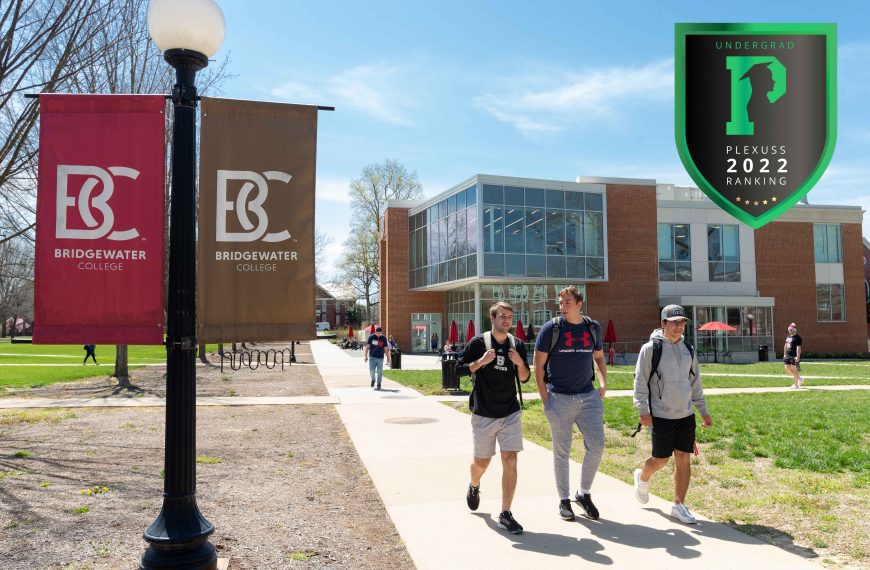 3 male students walk on campus. flags that say B-C are visible with the library in the background