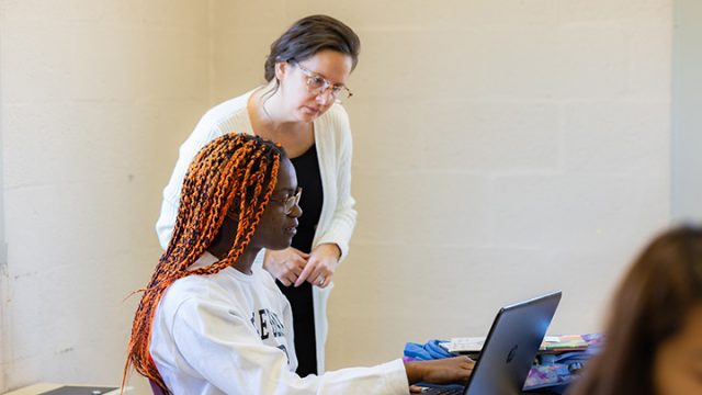 Professor helping students as they both look at a laptop