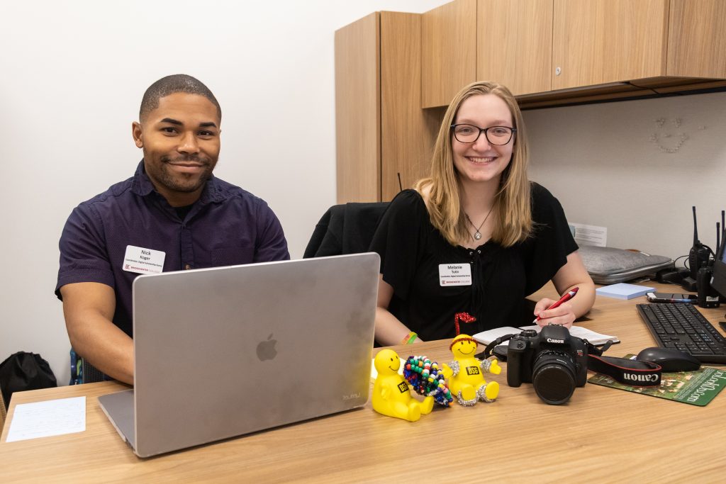 Two Digital Scholarship Guru student posing for picture in front of desk with laptop and camera 