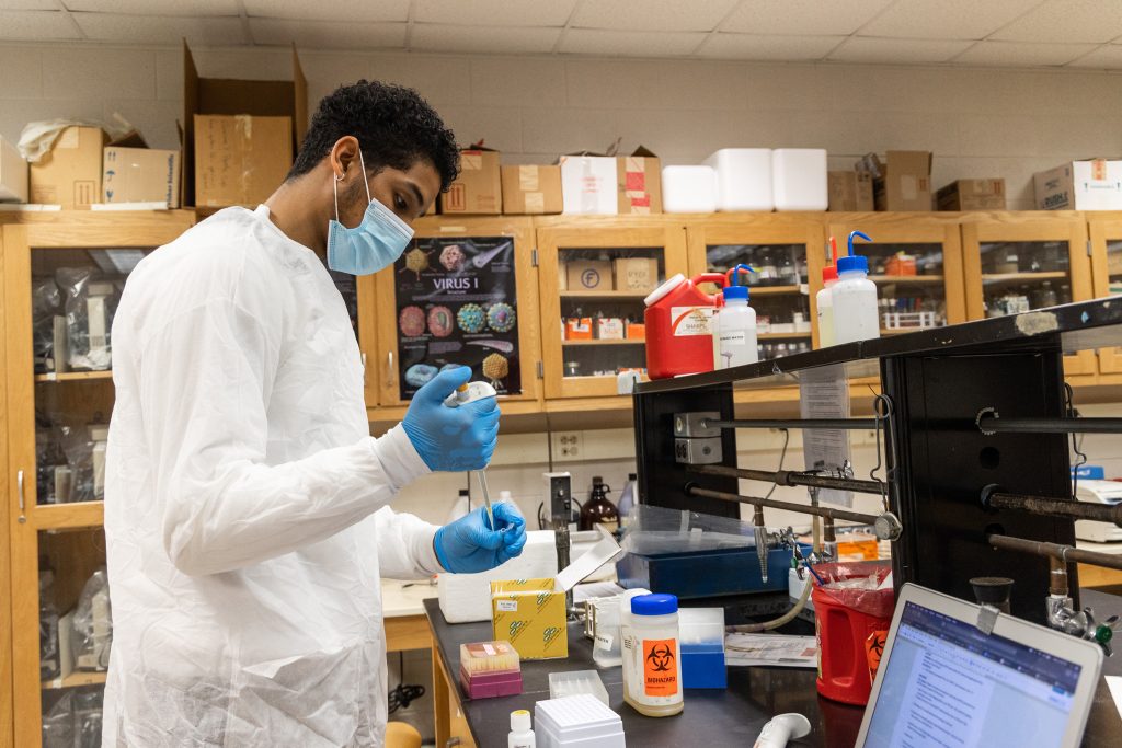 Student working with biology equipment in white gown and gloves