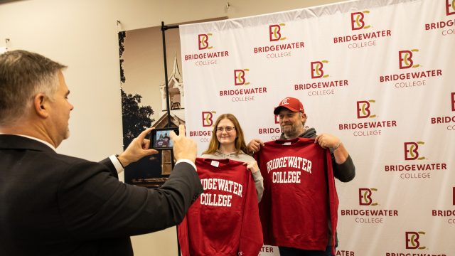 Father and daughter holding up Bridgewater College sweatshirts while someone takes a picture