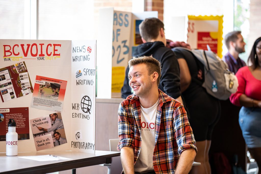 Student sitting in front of poster at club/org fair