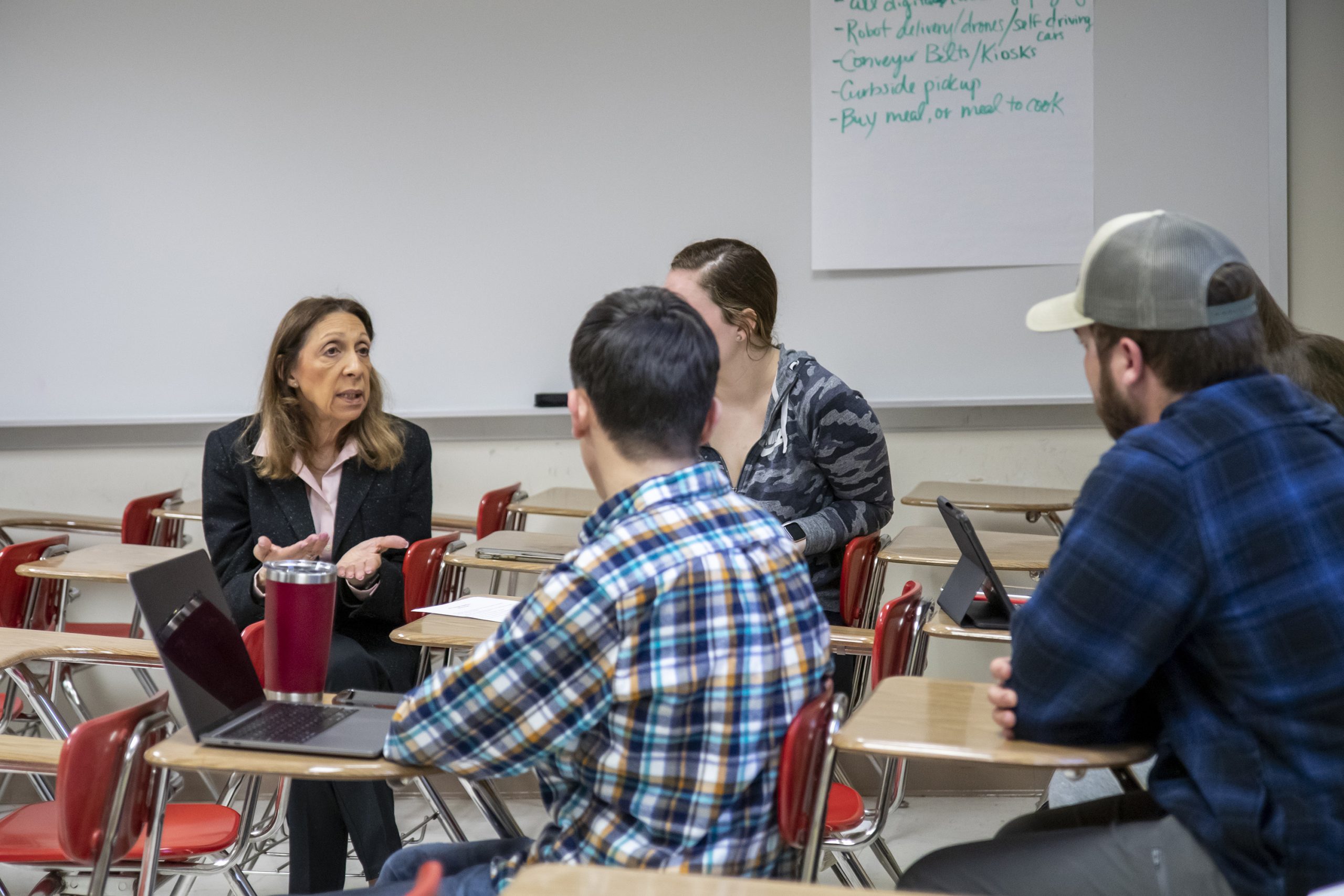 Professor sitting and talking with a group of students at desks