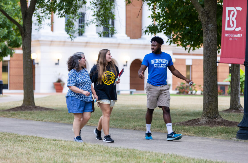 A Bridgewater employee wearing a blue Bridgewater College t-shirt taking a prospective student and her mom on a campus tour