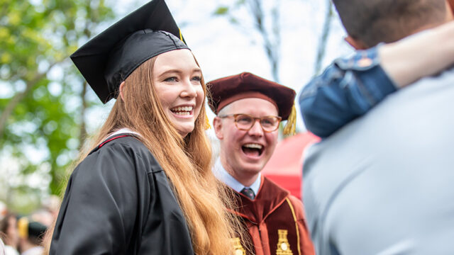 Professor and student smiling and laughing at commencement