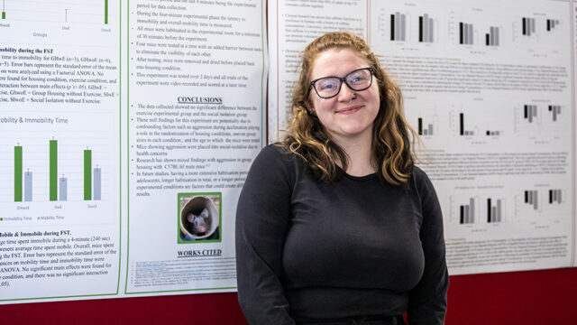 Student standing in front of presentation posters smiling