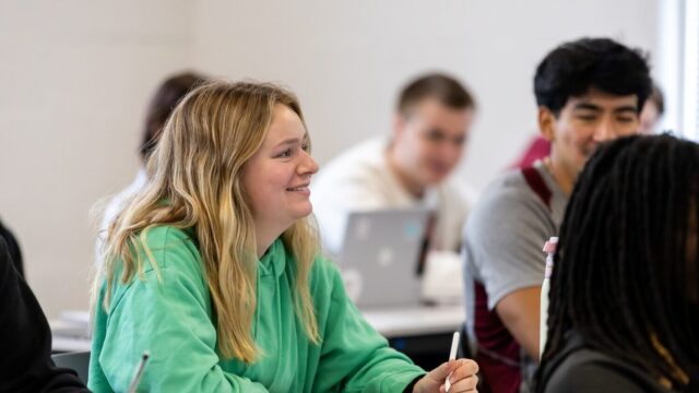 Girl sitting in class, smiling and holding a pencil