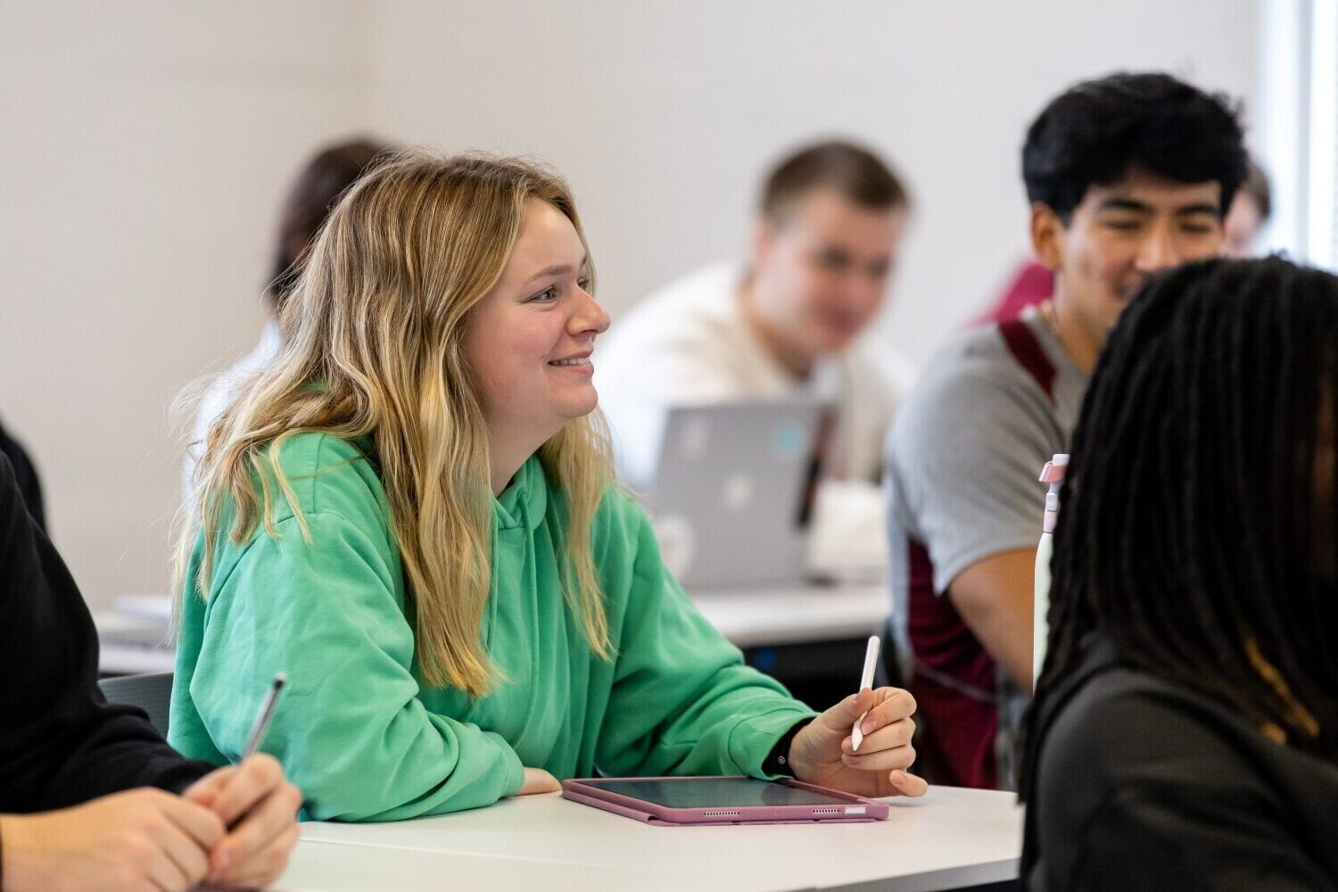 Girl sitting in class, smiling and holding a pencil