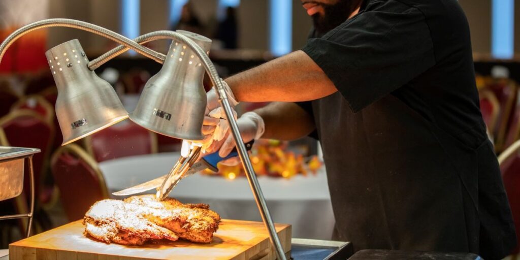 A chef carves a turkey under warmer lights